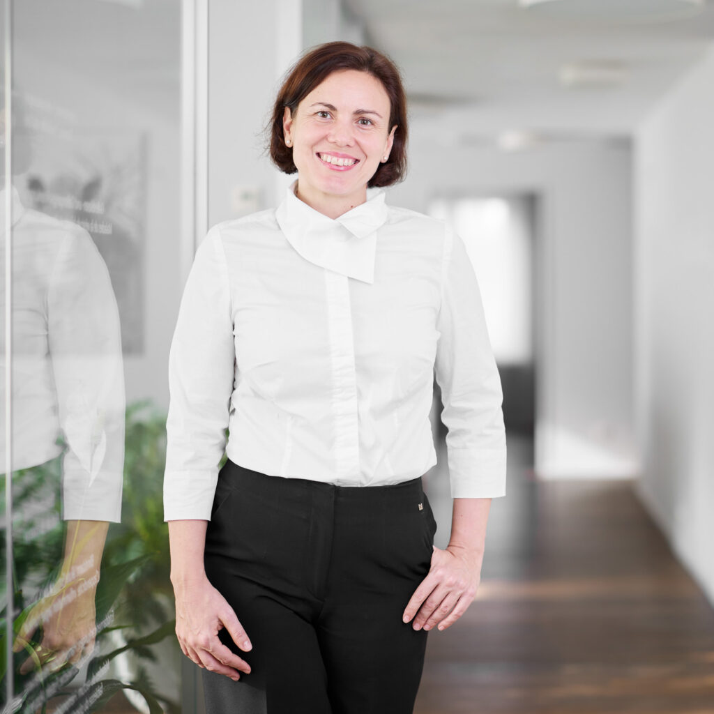 Ärztin steht in Gang in heller Praxis und lächelt in die Kamera