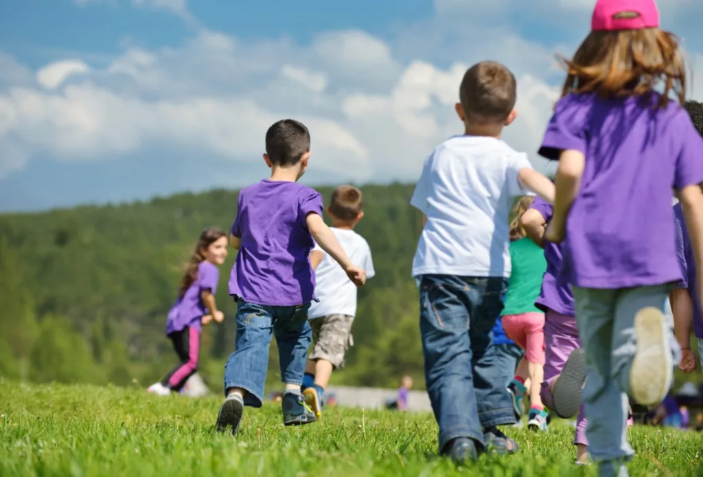 Mehrere Kinder laufen gemeinsam über eine Wiese im Freien und bewegen sich spielerisch in einer natürlichen Umgebung.