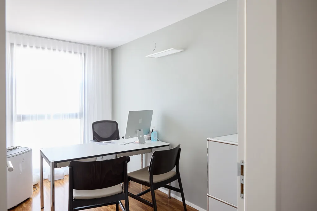 Heller Raum. Tisch mit Stühlen auf beiden Seiten. Computerbildschirm zu sehen.