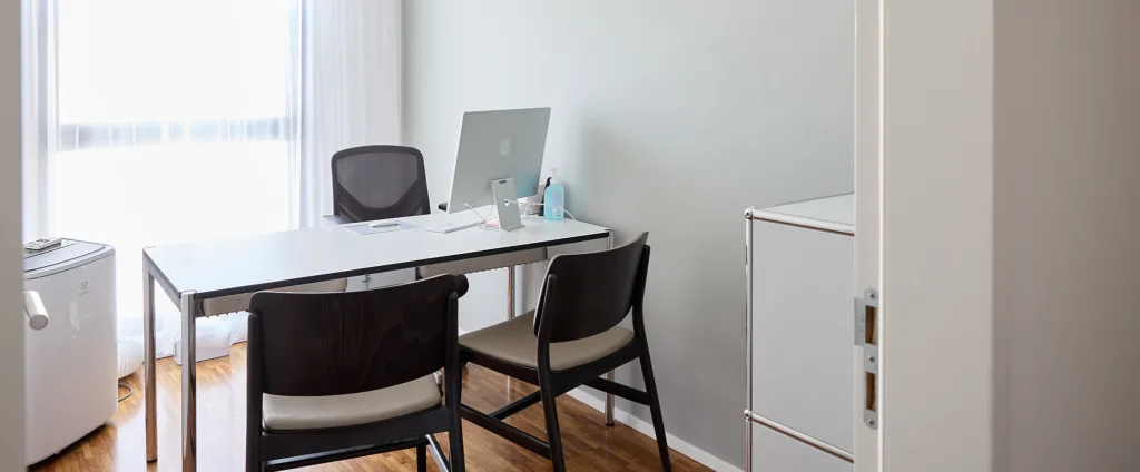 Heller Raum. Tisch mit Stühlen auf beiden Seiten. Computerbildschirm zu sehen.