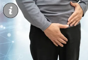 Bildausschnitt der Leiste eines Mannes, er trägt schwarze Hosen und graues Operteil. Fässt sich an Leiste und Bauch.